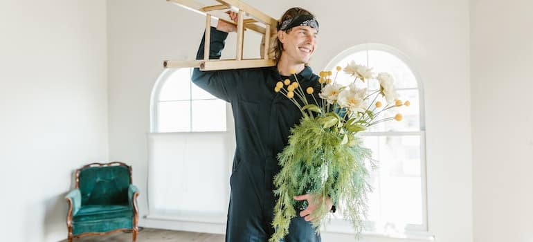 A proffesional mover holding a stool and a flower in a vase;