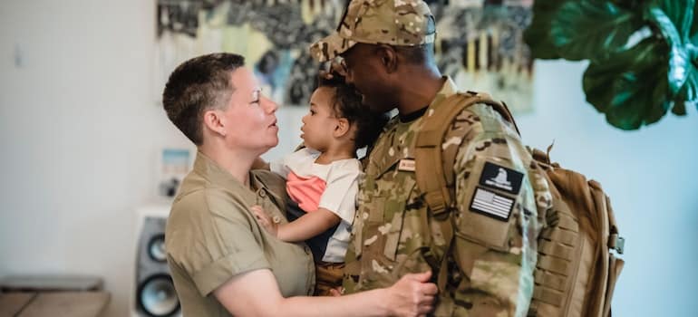 A woman carrying a child beside a man in military uniform