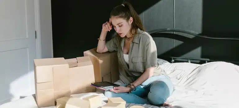 A woman on bed with lots of moving boxes around here, symbolising various moving day challenges.