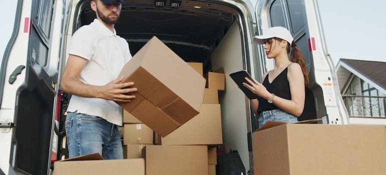 A man and a woman from a moving comapny packing moving boxes into a truck.