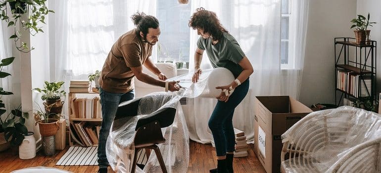 a couple wrapping the chair in bubble wrap and talking about why move designer furniture with white glove movers in Coconut Grove