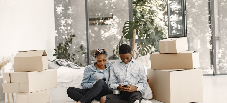 a man and a woman sitting on the floor, surrounded by packing boxes