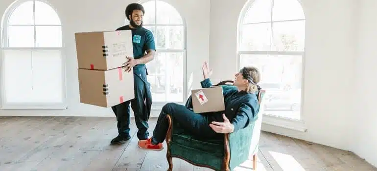 white glove movers, one standing and holding boxes, the other one sitting with a box in his lap