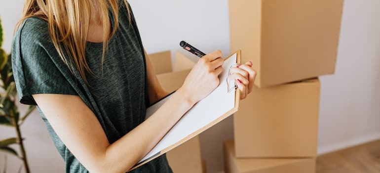 A woman writing something on a sheet of paper next to some moving boxes.