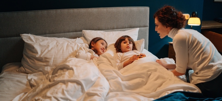 A woman talking to two small kids in bed