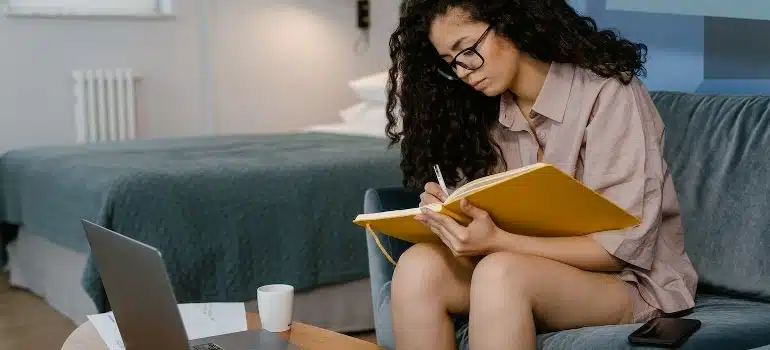 A young woman trying to evaluate a quality office moving company in Wynwood while writing in a notebook