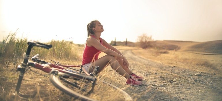 A woman sitting on the ground with a bike next to her 