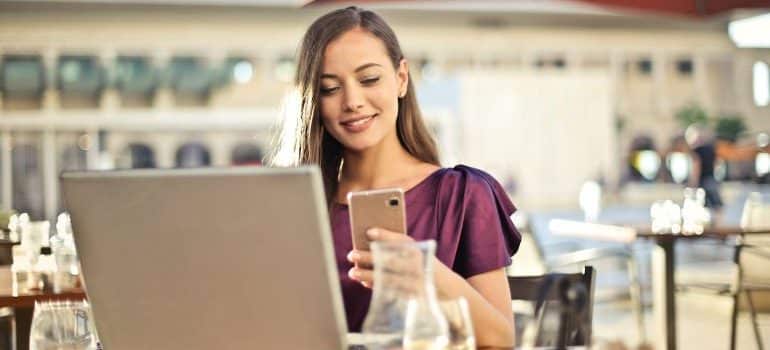 woma using a phone and a laptop in a restaurant