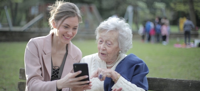 a mother and daughter sitting in a park using a smartphone