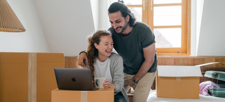 A happy couple surrounded by boxes using a laptop to make a plan for a last-minute art move