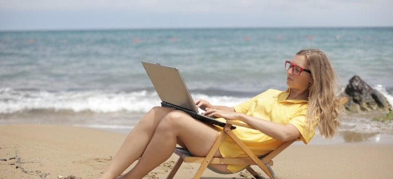 a woma sitting on the beach with a laptop searching for things to do in Golden Beach this summer