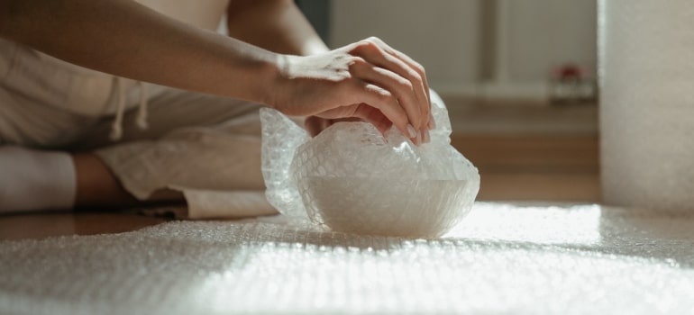 A person packing a bowl in a bubble wrap