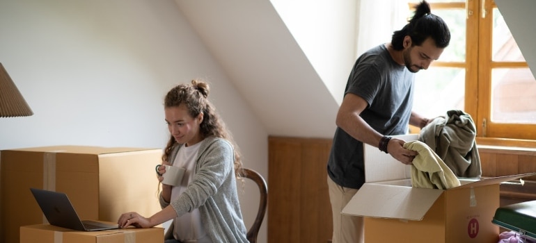 A man packing up a box and a woman searching the internet on ways to organize a small move in Kendall