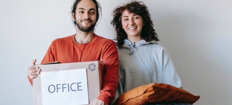 a man carrying a box labeled office and a woman carrying pillows