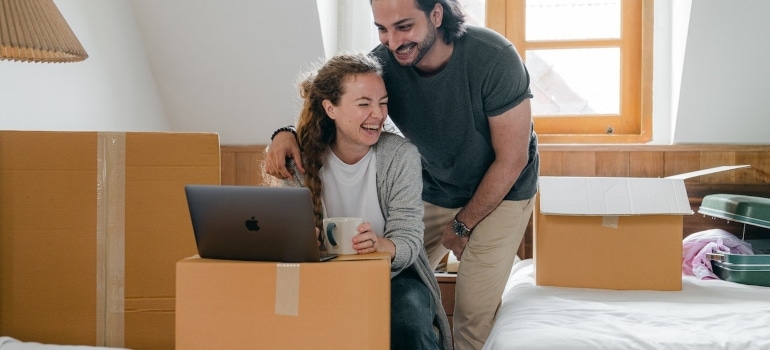 a couple with a laptop surrounded by boxes checking the differences in the cost of living before moving from Plantation to Pinecrest 