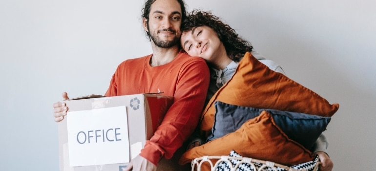 a man holding a box labeled office and a woman holding a basket of pillows