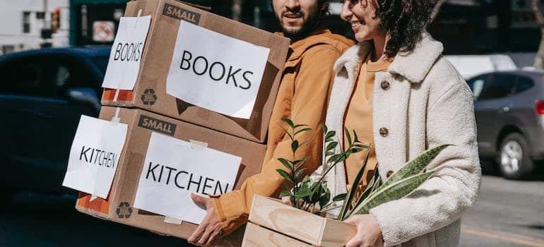 a man and a woman holding cardboard boxes and waling down the street