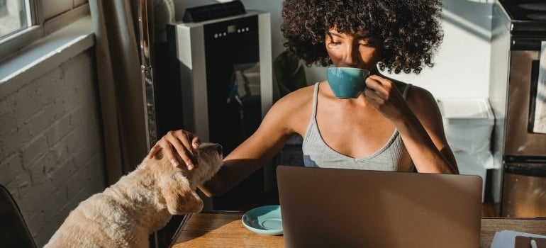 a woman drinking coffee with a dog next to her, searching the internet for a family with the dog in one ofMiami Neighborhoods for Pet-Friendly Living 