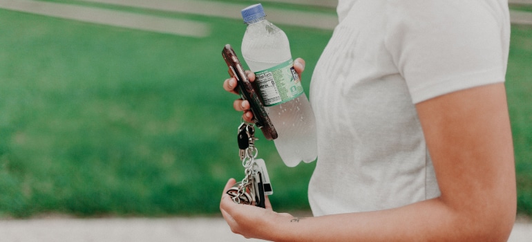 A girl holding a phone, keys and a bottle of water