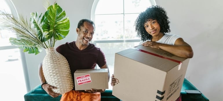 a man carrying a plant and a woman carrying a box