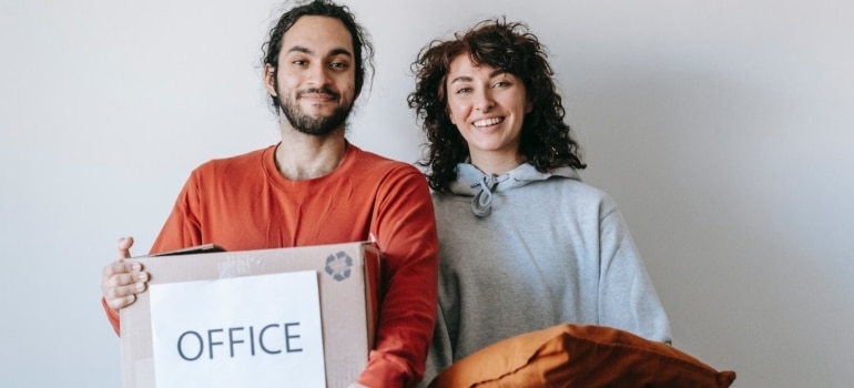 a man and an woman, the man is holdng a box labeled office and a woman is holding a pilloow