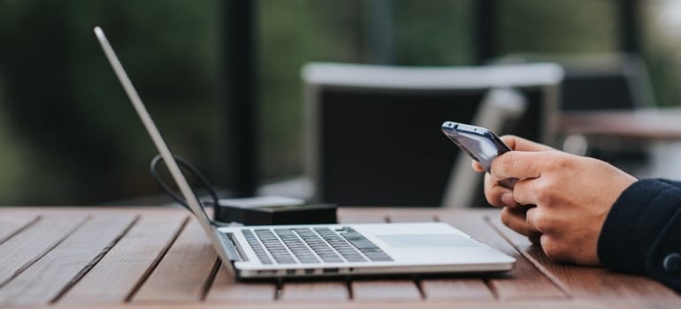 a man using a phone and a laptop searching for Job opportunities to expect after moving to Miami