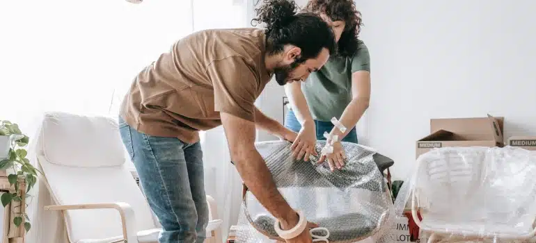 a couple using bubble wrap to pack wooden furniture 