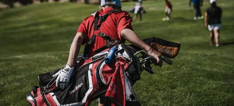 Man Walking Carrying Black and Red Golf Bag on Green Grass Field