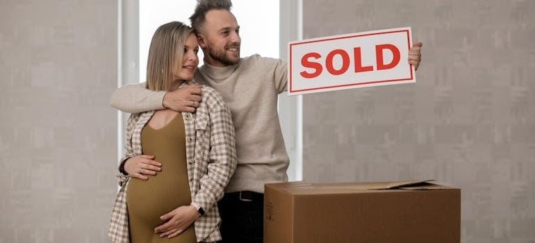 a pregnant woman and her partner holding a 'sold' sign