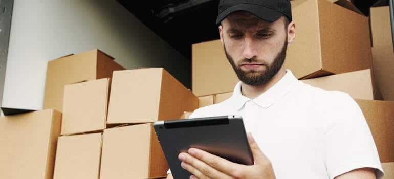 a man in front of a moving truck full of boxes checking inventory on a tablet