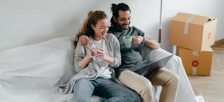 a happy couple looking at a laptop with boxes behind them