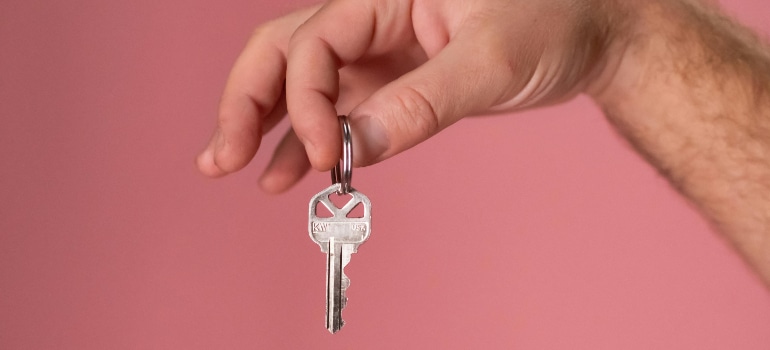 Hand holding a house key against a pink background, closing day moment for first-time homebuyers in Bal Harbour.