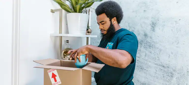 Mover cushioning a ceramic mug in a cardboard box at home, packing oddly shaped items for a long distance relocation.