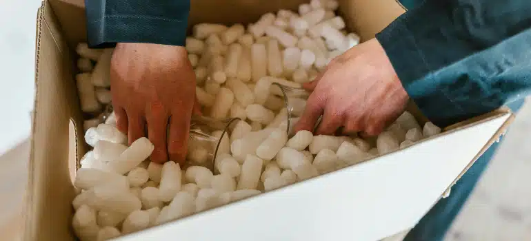 Close-up of hands securing glassware in a box filled with packing peanuts, packing oddly shaped items for a long distance relocation.