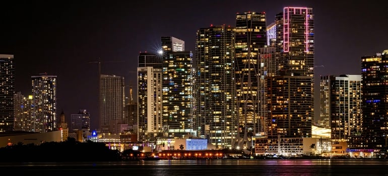 Miami skyline at night with lit towers and bay reflections, showing city energy to move to Wynwood in 2025.