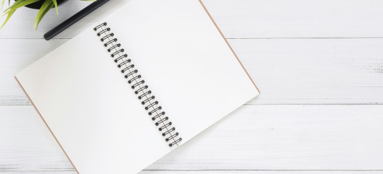 Open spiral notebook with pen on a white wood desk, ready for a checklist.