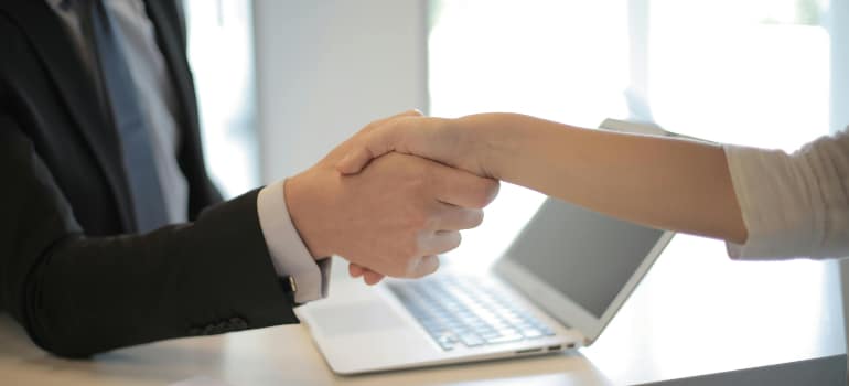 Close-up of a handshake over a laptop in a modern office, symbolizing a business deal or partnership.