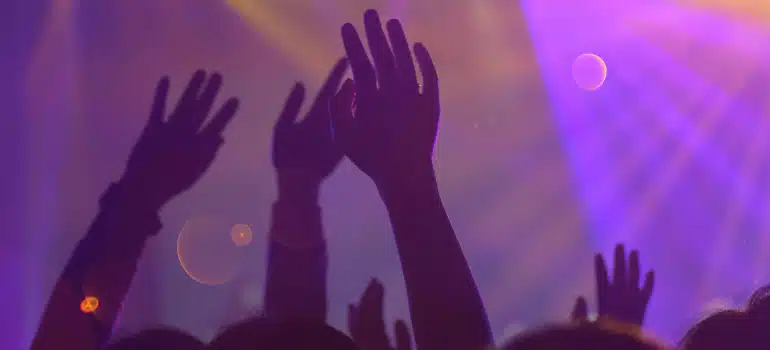 Crowd with raised hands under purple stage lights at a lively nightlife event or concert.