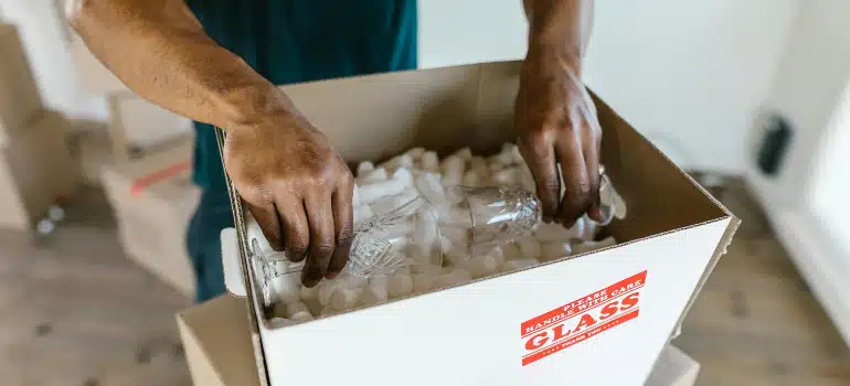 Hands placing a fragile glass vase into packing peanuts in a labeled box while packing oddly shaped items for a long distance relocation.