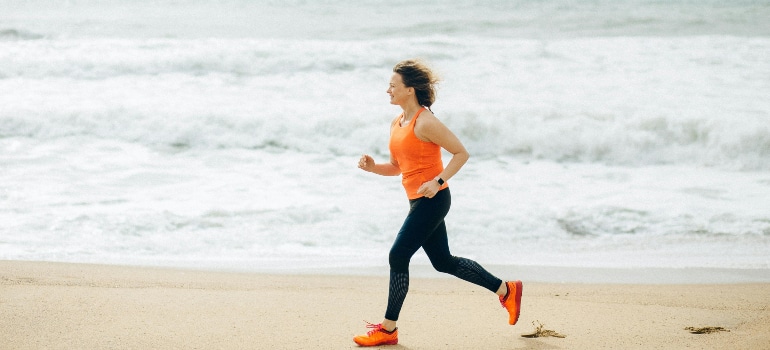 Woman jogging on wet sand with waves rolling in at top outdoor exercise parks in Miami.