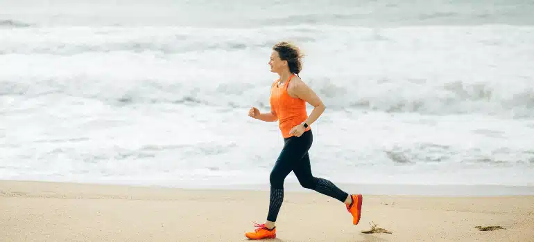 Woman jogging on wet sand with waves rolling in at top outdoor exercise parks in Miami.