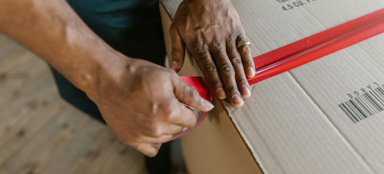 Hands applying red packing tape to secure a moving box.