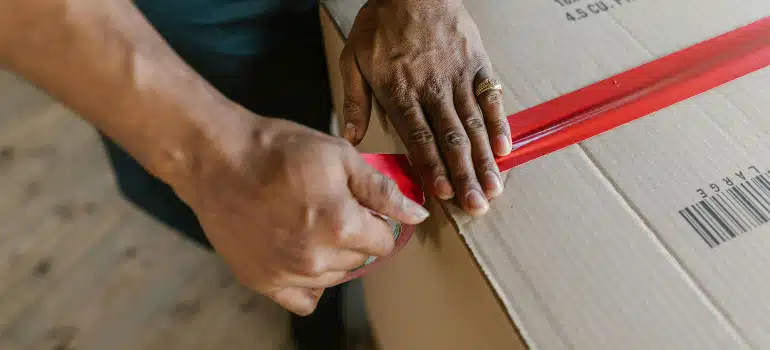 Hands applying red packing tape to secure a moving box.