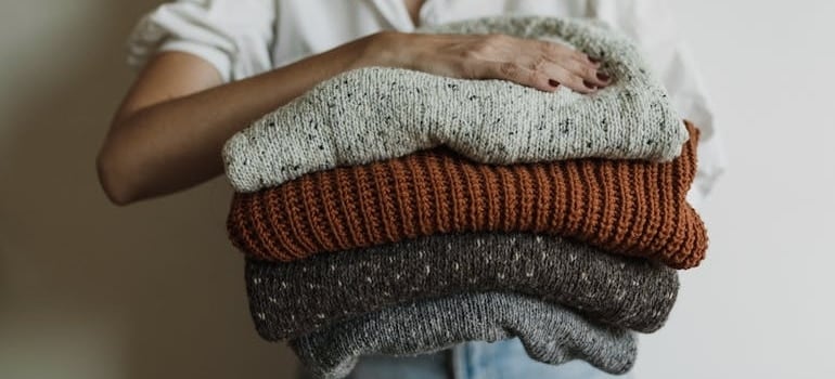 Woman Holding Pile of Knitted Sweaters